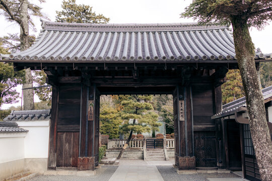 Traditional Japanese wooden gate with tiled roof amidst greenery and stone path. Kyoto, Japan