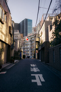 Quiet urban street with shadowed buildings and a distant Japanese flag hanging high. Tokyo, Japan