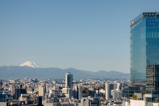 Urban skyline with a glass skyscraper and Mount Fuji in the background on a clear day. Tokyo, Japan