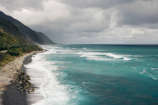 Dramatic cloudy sky over a rocky coastline with turquoise waves crashing onto the shore. Fengbin Township, Taiwan