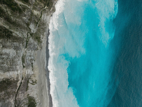 Aerial view of turquoise ocean waves crashing against a rugged cliffside shore. Coastline of Hualien County, Xiulin Township, Taiwan