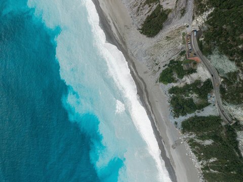 Aerial view of a vibrant coastline with turquoise waves crashing onto a sandy beach lined by cliffs. Coastline of Hualien County, Xiulin Township, Taiwan