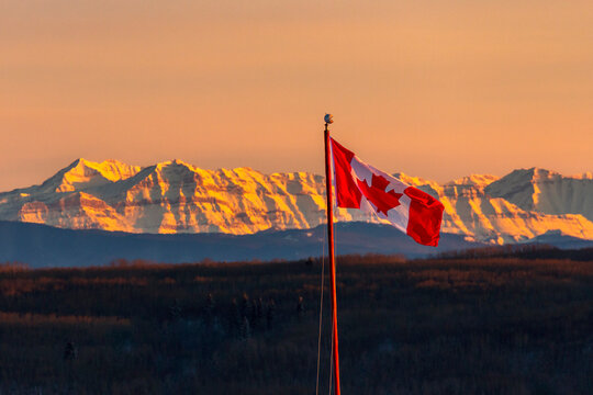 Canadian flag waving against a backdrop of mountains at sunset. Calgary, Canada