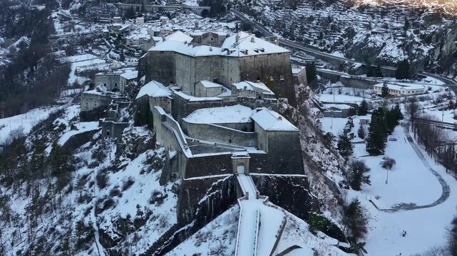 Aerial view of Forte di Exilles, an imposing snow-covered fortress perched high amidst a landscape of winter, Exilles, Piemonte, Italy.