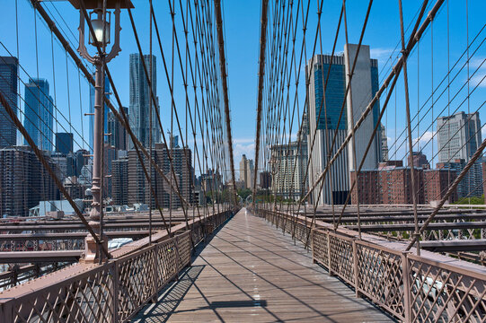 View of Brooklyn Bridge walkway with city skyline under a clear blue sky. New York, USA