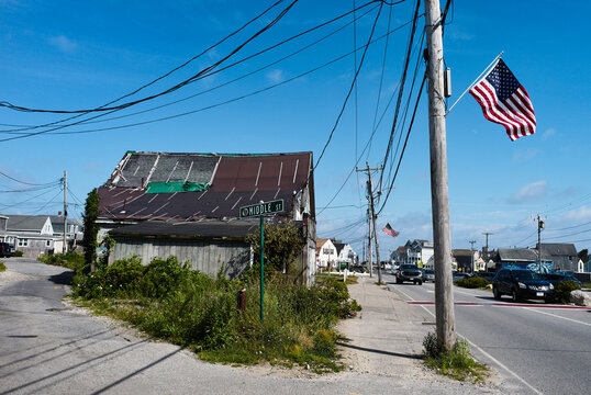 Street scene with weathered buildings, power lines, and American flags under a blue sky. Marshfield, USA