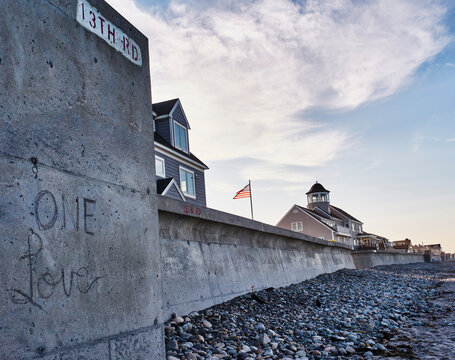 Seaside homes with an American flag and graffiti on a concrete wall under a cloudy sky. Marshfield, MA, USA