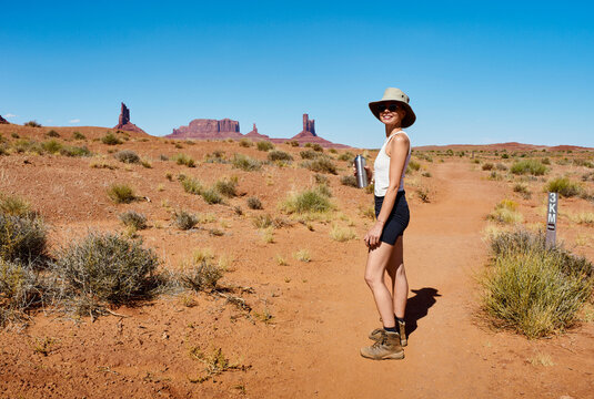Woman hiking a desert trail with rock formations and blue sky in the background. Monument Valley, Arizona, USA