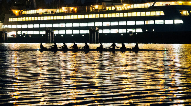 A rowing team silhouetted against a ferry on a shimmering body of water at night. WA, USA