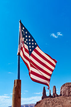 American flag waving against a clear blue sky, with rocky formations in the background. Monument Valley, Arizona, USA