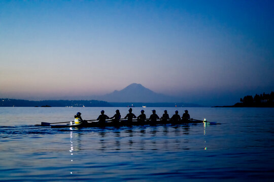 Rowing team gliding on calm water during twilight with mountain silhouette in the background. WA, USA