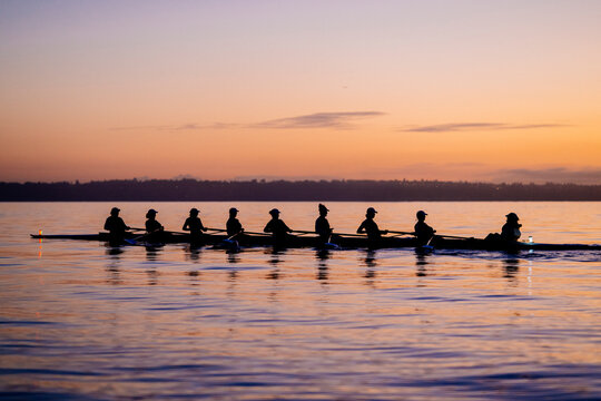 Rowing team silhouetted against a colorful sunset sky on calm water. WA, USA