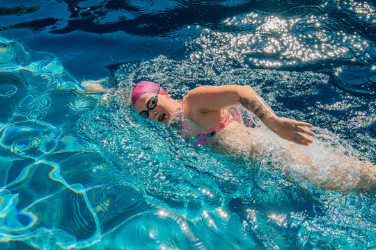 Swimmer wearing pink cap and goggles swimming freestyle in a bright blue pool. USA
