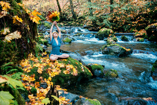 Woman meditating with autumn leaves beside a flowing stream in a forest setting. Washington State,,USA