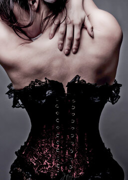 A woman in a corset, with her hands on her back.