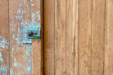 Close-up of an old wooden door with a vintage metal latch, peeling turquoise paint, and natural wood grain. Rustic texture background showing weathered surface, aged details, and traditional craftsman