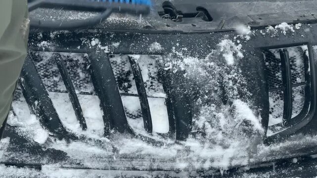 A man clears snow from a car. The car is covered in snow.
