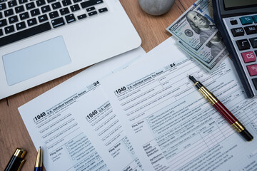1040 Tax preparation workspace with laptop calculator pen and dollar banknotes on wooden desk