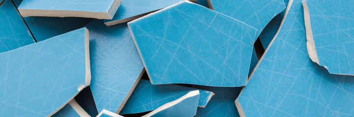 Heap of cracked blue ceramic wall or floor tiles background. Closeup. Wide banner. Top down view.