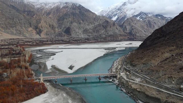 Aerial view of bridge with blue water flowing beneath it, surrounded by majestic mountains, creating a breathtaking landscape, Daghoni Balgar, Pakistan.