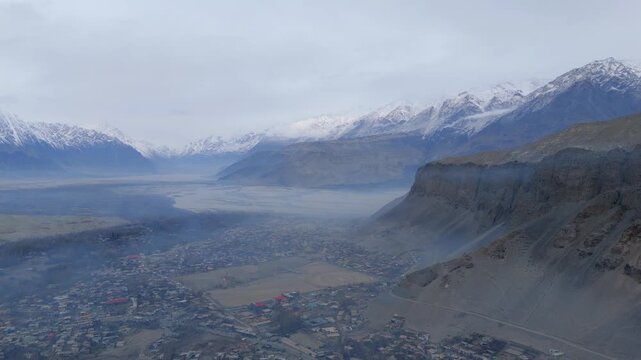 Aerial view of Skardu city nestled between rugged, snow-capped mountains under a hazy sky, creating a serene yet dramatic landscape, Skardu, Gilgit Baltistan, Pakistan.