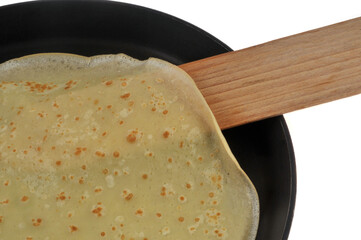 D&eacute;tail d'une cr&ecirc;pe bretonne dans une po&ecirc;le avec une spatule en bois en gros plan