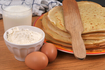 Pile de cr&ecirc;pes bretonnes dans une assiette avec une spatule en bois et ses ingr&eacute;dients