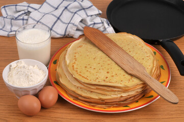 Pile de cr&ecirc;pes bretonnes dans une assiette avec une spatule en bois et ses ingr&eacute;dients