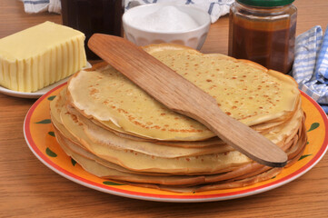 Assiette de cr&ecirc;pes bretonnes avec une spatule en bois, du beurre, du sucre, de la confiture et du caramel
