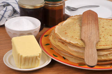 Assiette de cr&ecirc;pes bretonnes avec une spatule en bois, du beurre, du sucre, de la confiture et du caramel