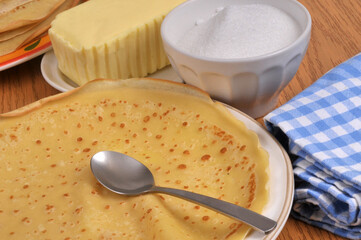 Cr&ecirc;pe dans une assiette avec une cuill&egrave;re, du beurre et du sucre en poudre au second plan