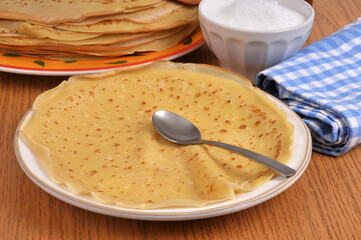 Cr&ecirc;pe dans une assiette avec une cuill&egrave;re et du sucre en poudre au second plan