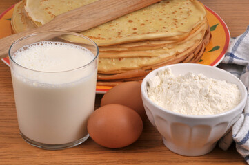 Pile de cr&ecirc;pes bretonnes dans une assiette avec une spatule en bois et ses ingr&eacute;dients