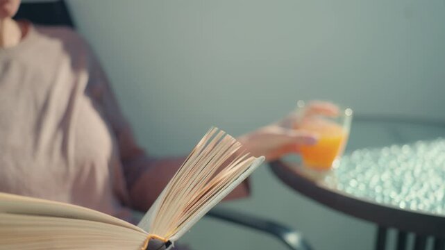 Woman enjoy read book and fresh orange juice on terrace in spring sunlight close up.Spring lifestyle concept, renewal and freshness, healthy habits,calm mood,natural daylight, seasonal everyday moment