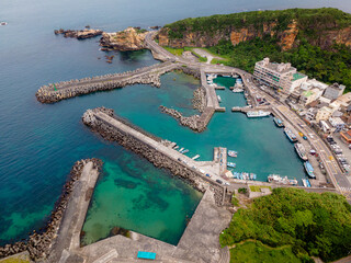 Aerial view of Wanli Fishing Harbor in Taiwan, showing a small harbor sheltered by multiple concrete piers, surrounded by clear blue ocean water and a rugged coastal setting.

