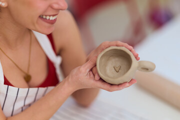 Happy Woman Crafting Heart-Shaped Clay Mug During Pottery Studio Workshop With Apron