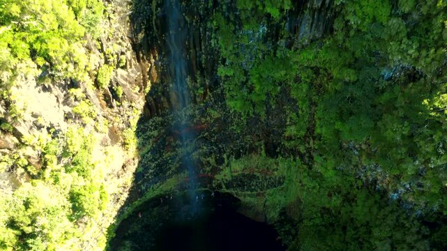 Aerial establishing shot of Lagoa do Vento waterfall in Madeira, drone rising with tilt down revealing hikers walking behind the water flow and hidden lagoon in Rabacal mountains, travel adventure.