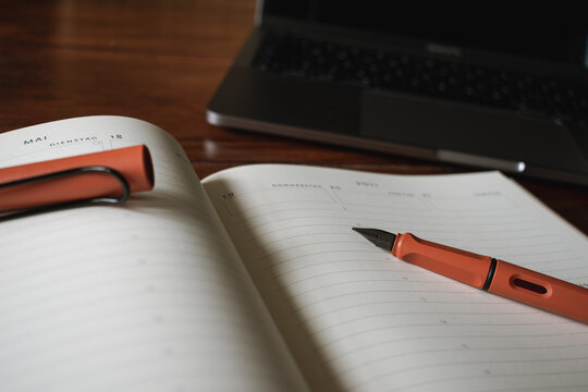 analoger Terminkalender mit orangenem F&uuml;ller vor einem Laptop im Homeoffice