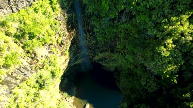 Aerial establishing shot of Lagoa do Vento waterfall in Madeira, drone rising with tilt down revealing hikers walking behind the water flow and hidden lagoon in Rabacal mountains, travel adventure.