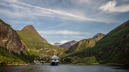 View from Geirangerfjord toward the village of Geiranger, Norway, on a clear summer day. A cruise ship docked at the pier.