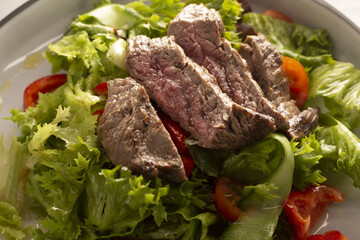Fototapeta premium Sliced steak over mixed greens salad. Seared beef slices arranged on bed of lettuce and tomato with light vinaigrette, charred crust and pink center visible proteinpacked restaurant plate, upscale