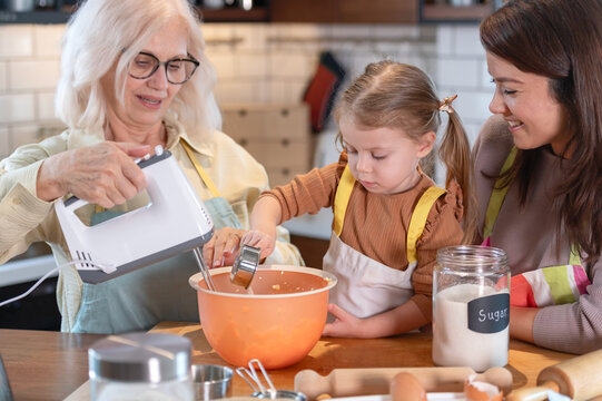 Grandmother, mother, and young daughter bake together in a home kitchen, mixing ingredients and measuring sugar, capturing family bonding, generations cooking, learning, and warm everyday moments