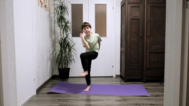 Caucasian boy stepping in place lifting his knee to elbow. Child doing sport exercise at home. Children workout. Strengthening the muscles. Strong sporty body. Active healthy lifestyle. 4k footage.