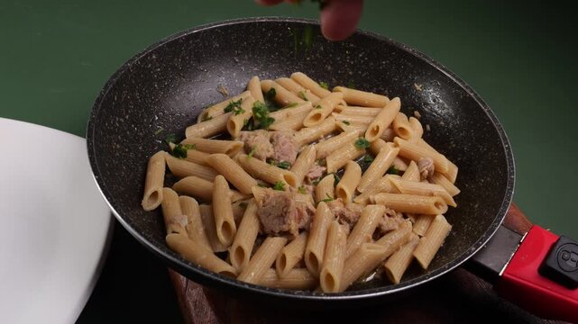 Cuoco mette il prezzemolo nella pasta al tonno e limone ancora nella padella
