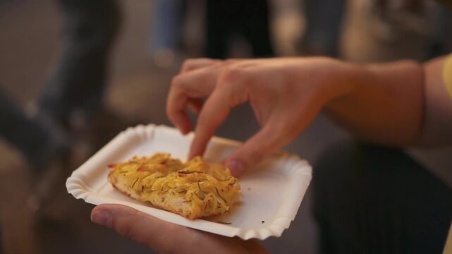 Close-up of hands holding a slice of traditional Italian pizza al taglio served on a paper plate. Street food takeaway scene in Rome, Italy, showing authentic local cuisine and casual eating during