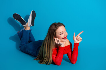 Young fashionable woman pointing with a joyful expression on bright blue background, emphasizing...