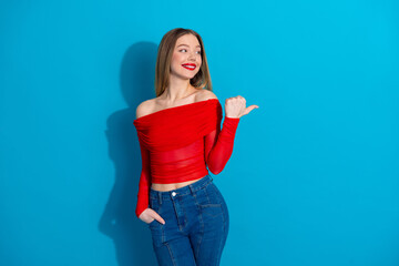 Stylish young woman in a red top and jeans posing confidently against a vibrant blue background...