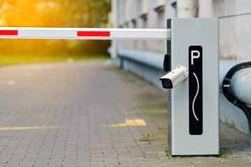 Automatic boom barrier for parking lot management with monitoring camera. Automatic security gate with striped arm, integrated surveillance camera providing restricted access to private parking area