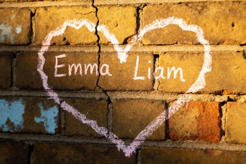 Pink chalk heart on brick wall with names symbolizing love.