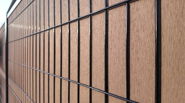 Slow panning shot showing the texture of WPC composite wood slat mounted on a rigid black metal fence, highlighting material detail and modern design.